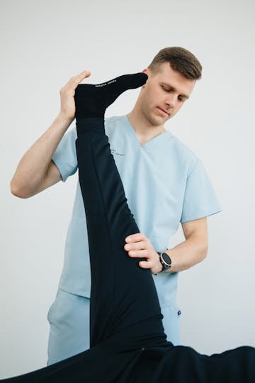 Physiotherapist guiding a patient through a supported leg stretch during treatment